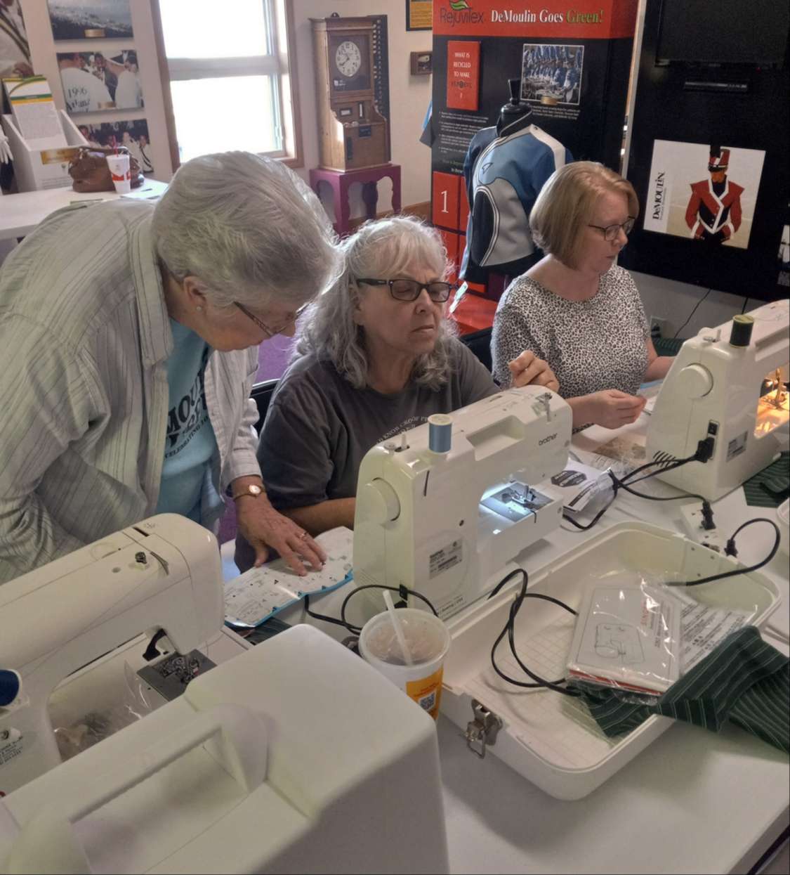 three mature women at a table of three white sewing machines