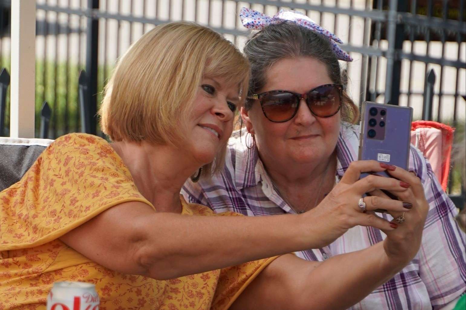 blond woman takes a phone selfie with a woman wearing sunglasses
