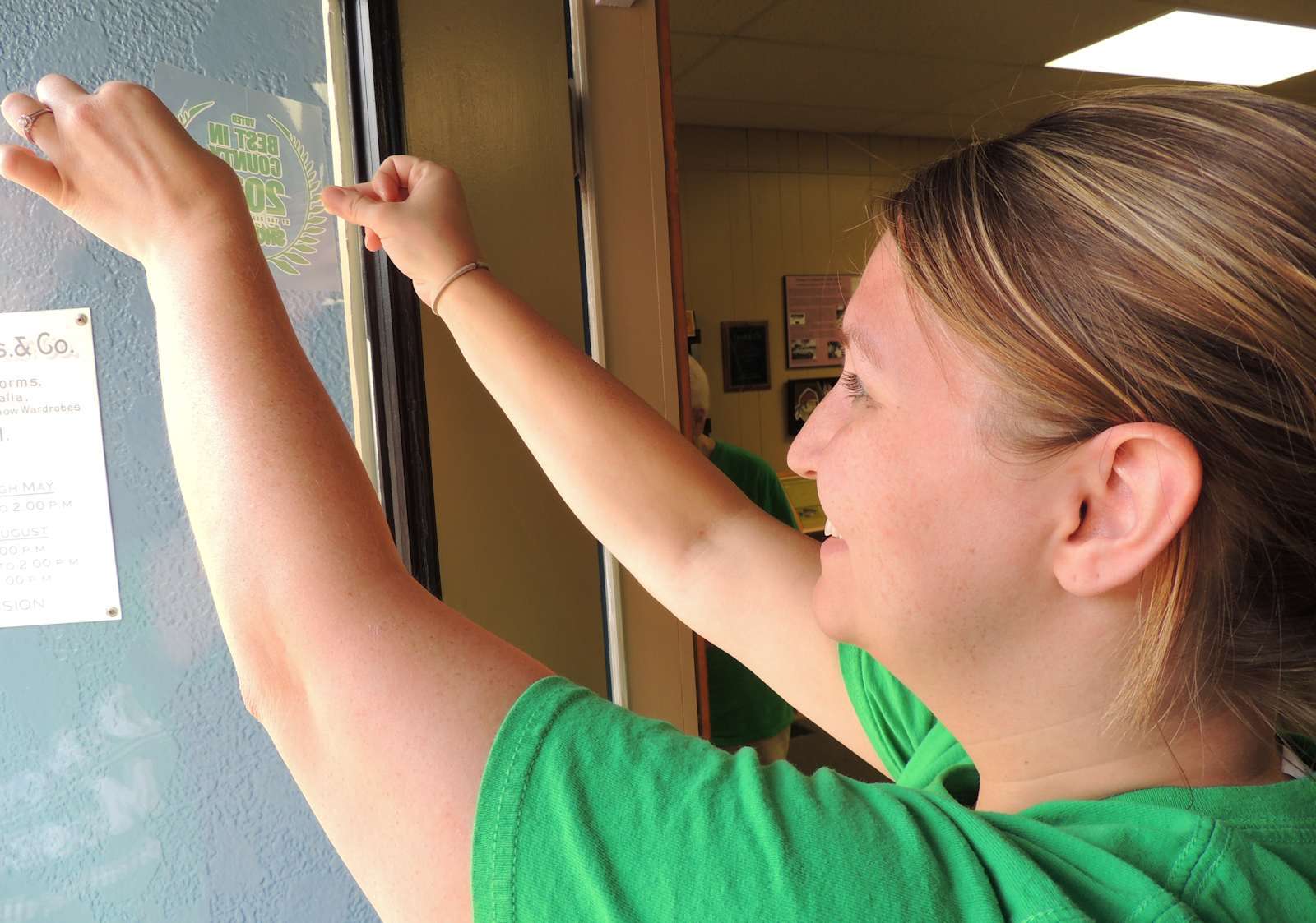 DeMoulin Museum volunteer Gina Lewis afixes window cling announcing Shopper Award status.